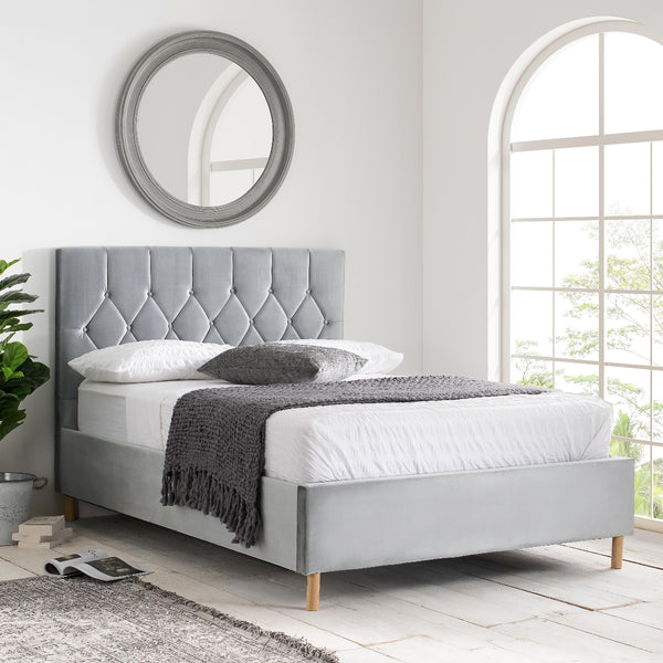 Gray upholstered bed in a bright room with a mirror and window.