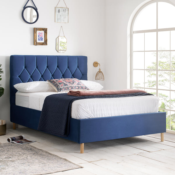 Blue upholstered bed in a bright bedroom with large windows.