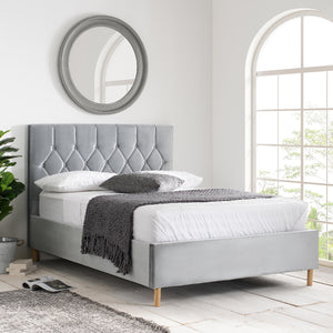 Gray upholstered bed in a bright room with a mirror and window.