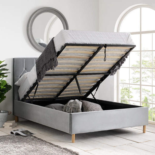 Gray upholstered bed with open storage compartment in a bright room.