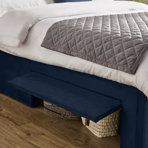 Navy blue bed skirt on a bed with white bedding and a gray quilt.