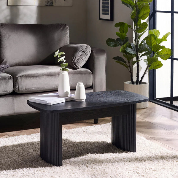 Modern living room with a gray sofa, black coffee table, and decorative plants.