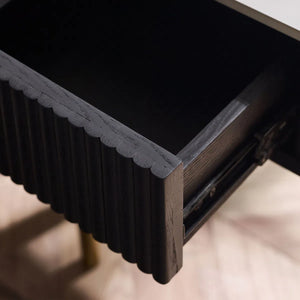 Close-up of a dark wooden drawer with scalloped edge on a light-colored surface.