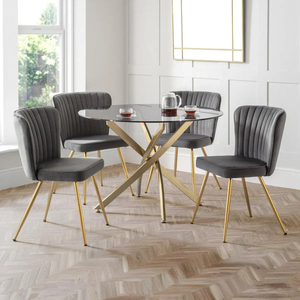 GREY MONZA DINING CHAIR WITH GOLD LEGS AROUND A GLASS TABLE WITY GOLD LEGS IN A DINING ROOM SETTING