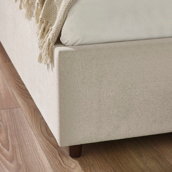 Beige upholstered bed with wooden legs on a wooden floor