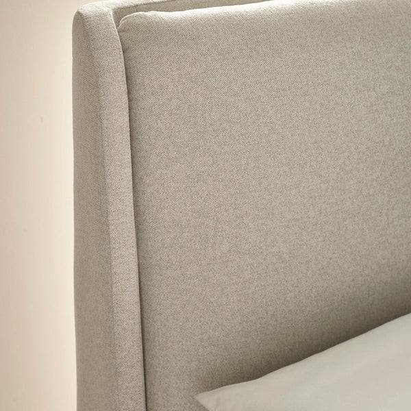 Close-up of a beige upholstered headboard with a pillow.