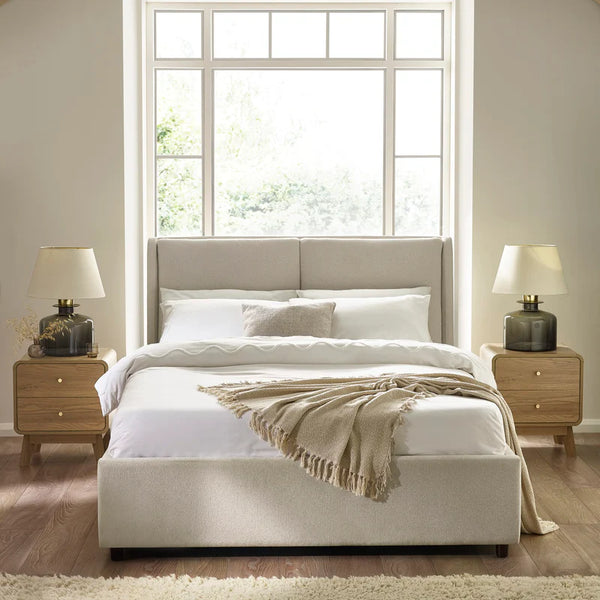 Neatly made bed with beige headboard and bedding in a bright bedroom.