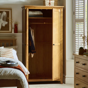 Wooden wardrobe in a bedroom with open doors, showing clothes inside.