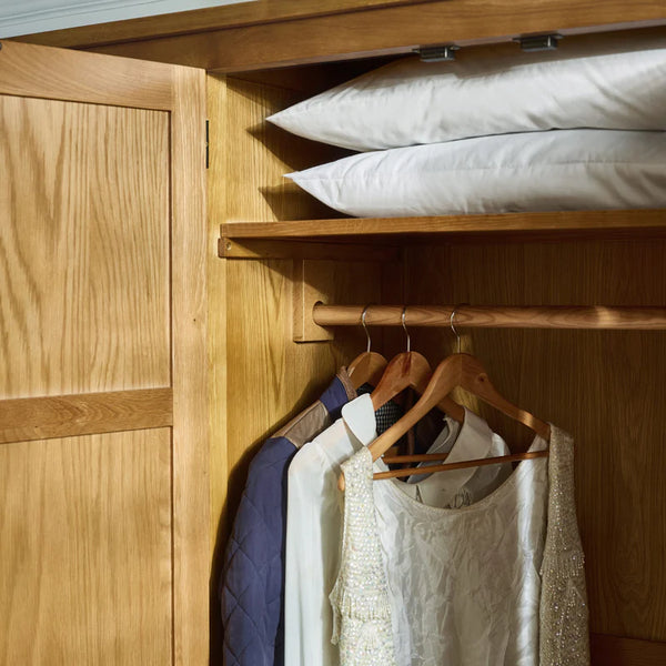 Wooden wardrobe with clothes on hangers and pillows on a shelf