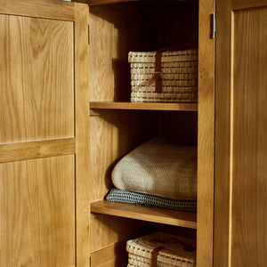 Wooden wardrobe with shelves containing pillows and a woven basket.
