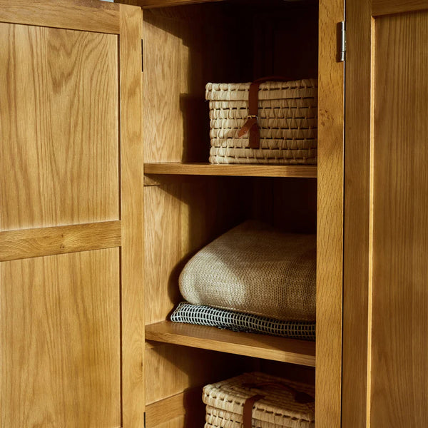 Wooden wardrobe with shelves containing pillows and a woven basket.