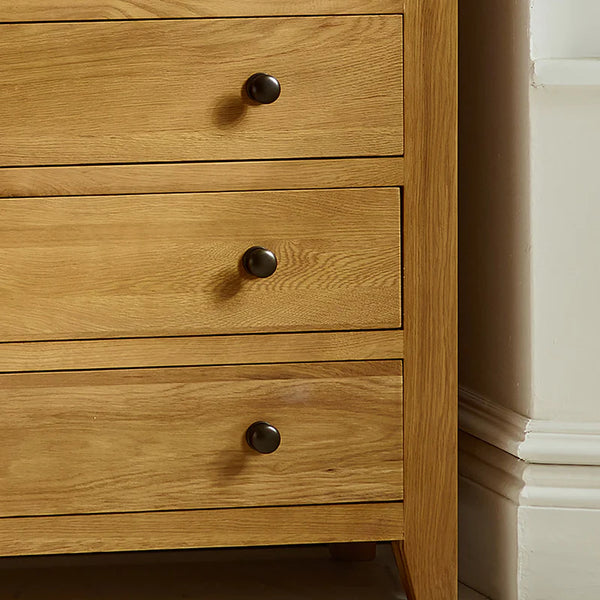 Wooden dresser with three drawers and metal knobs in a neutral setting.