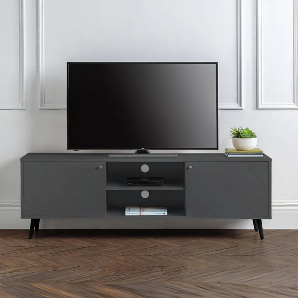 Gray TV stand with a television and decorative items in a room with white walls and wooden flooring.
