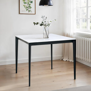 White table with black legs in a room with light wood flooring and a window.