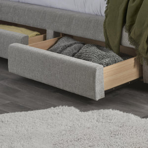 Gray upholstered bed with open drawer revealing gray pillows on a wooden floor.
