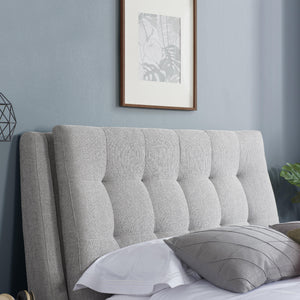 Gray upholstered headboard with pillows against a light blue wall with framed art.