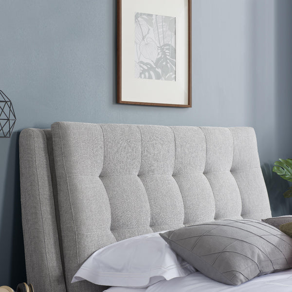 Gray upholstered headboard with pillows against a light blue wall with framed art.