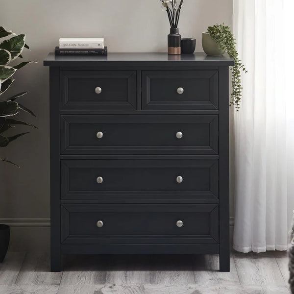 Black dresser with silver knobs in a room with plants and a curtain.