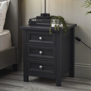 Black nightstand with three drawers next to a bed in a bedroom setting.