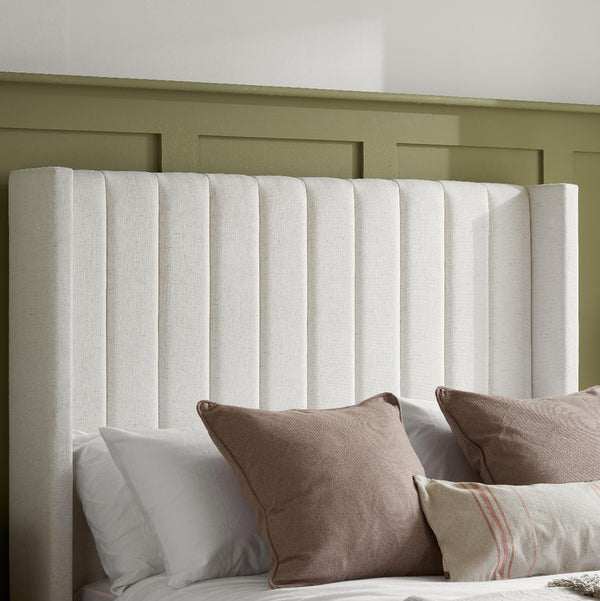 White upholstered headboard with brown and white pillows against a green wall.