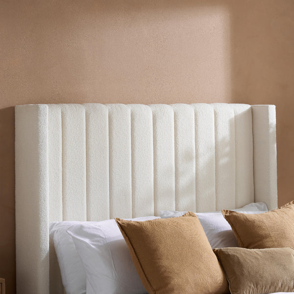 White upholstered headboard with brown pillows against a beige wall