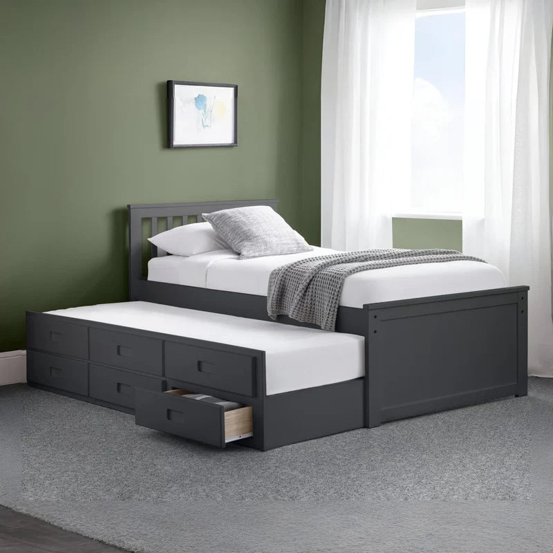 Gray bed with white bedding and pull-out drawer in a room with green walls and a window.