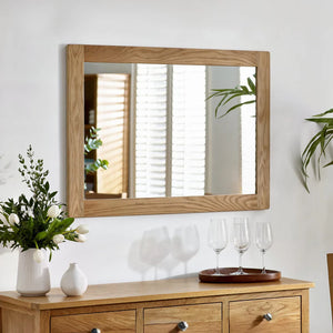 Wooden dresser with mirror, flowers, and glasses on a white wall.