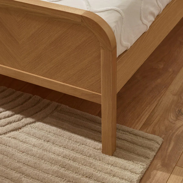 Wooden bed frame with a textured rug on a wooden floor