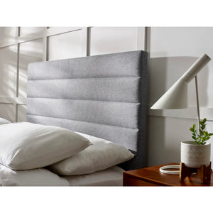 Gray upholstered headboard with white pillows and a wooden nightstand in a bedroom setting.