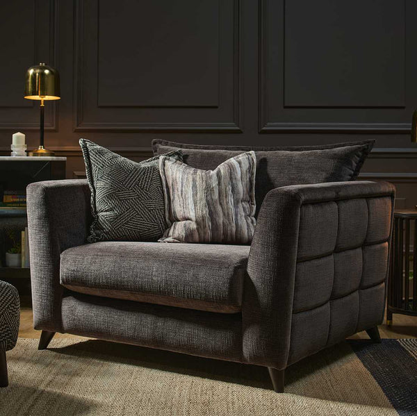 Gray armchair with patterned cushions in a darkly paneled room.