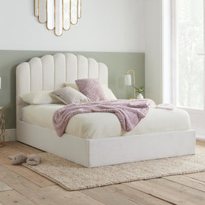 White upholstered bed with pink blanket and pillows in a bedroom setting.