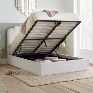 White bed with open storage compartment in a room with light wood flooring and a window.