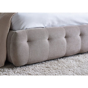 Beige tufted footboard on a bed with white bedding