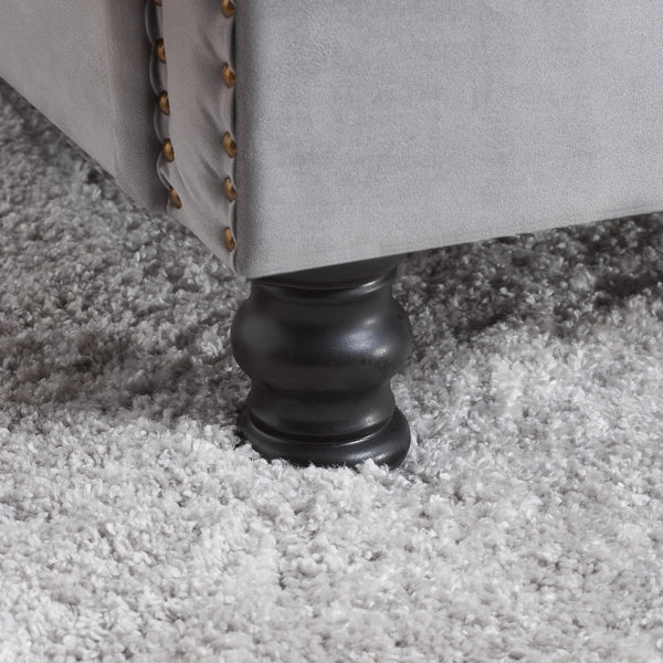 Close-up of a gray upholstered bed leg on a carpeted floor