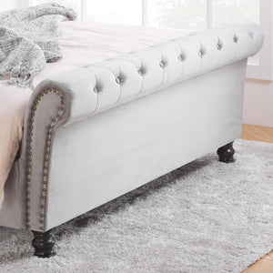 Gray upholstered bed with tufted footboard and nailhead trim on a gray rug.