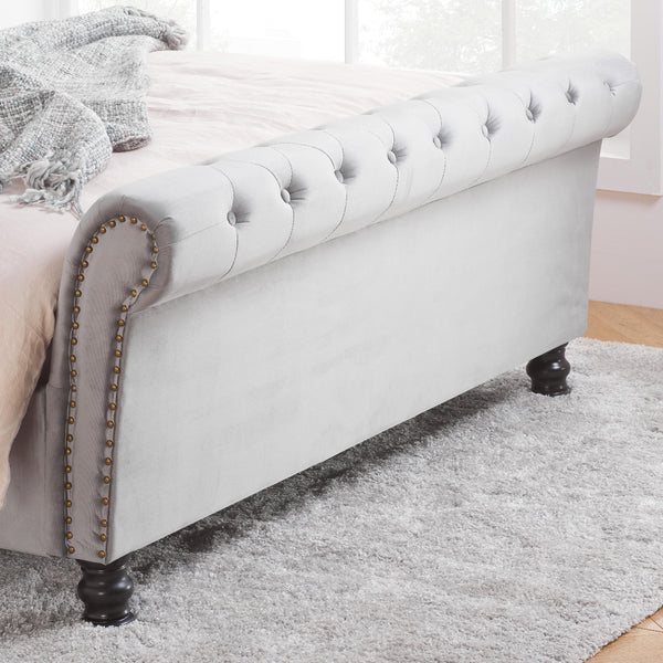Gray upholstered bed with tufted footboard and nailhead trim on a gray rug.