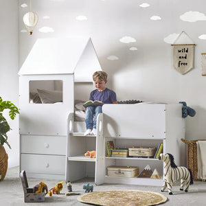 Child reading a book in a white children's room with a playhouse bed.