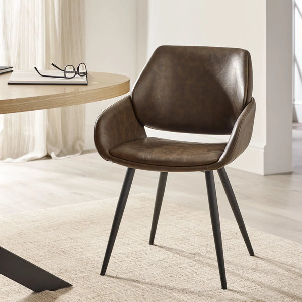 Brown leather chair with black metal legs in a room with a desk and curtains.