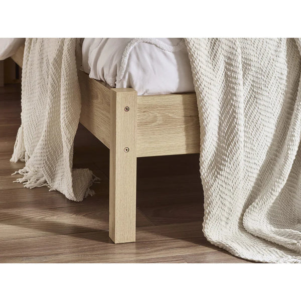 Wooden bed frame with white bedding and a textured beige blanket on a wooden floor.