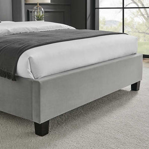 Gray upholstered bed with white bedding in a room with large windows.