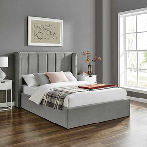 Gray upholstered bed in a bedroom with a window and wall art.