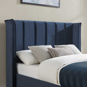 Blue upholstered bed with white bedding and decorative pillows against a beige wall.