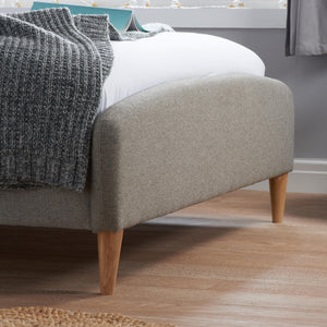 Gray upholstered bed with wooden legs in a room setting