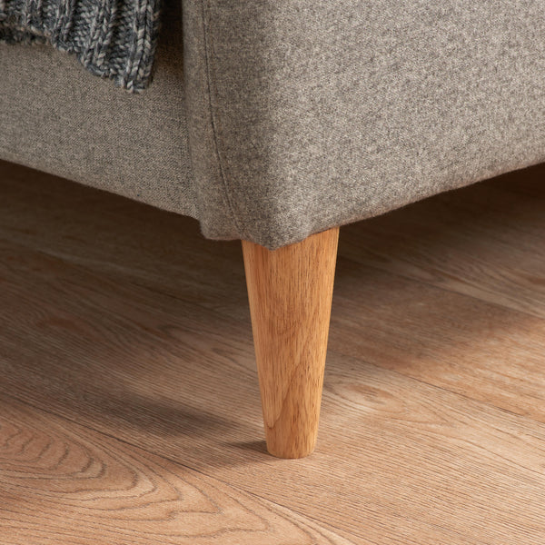 Close-up of a gray upholstered bed with a wooden leg on a wooden floor.