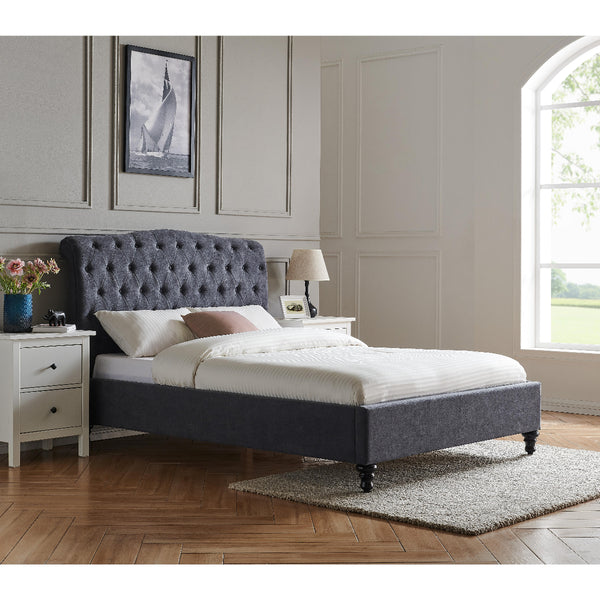 Gray upholstered bed in a bedroom with white walls and a window.