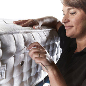 Woman hand side stitching a mattress with a close-up view of the mattress surface.