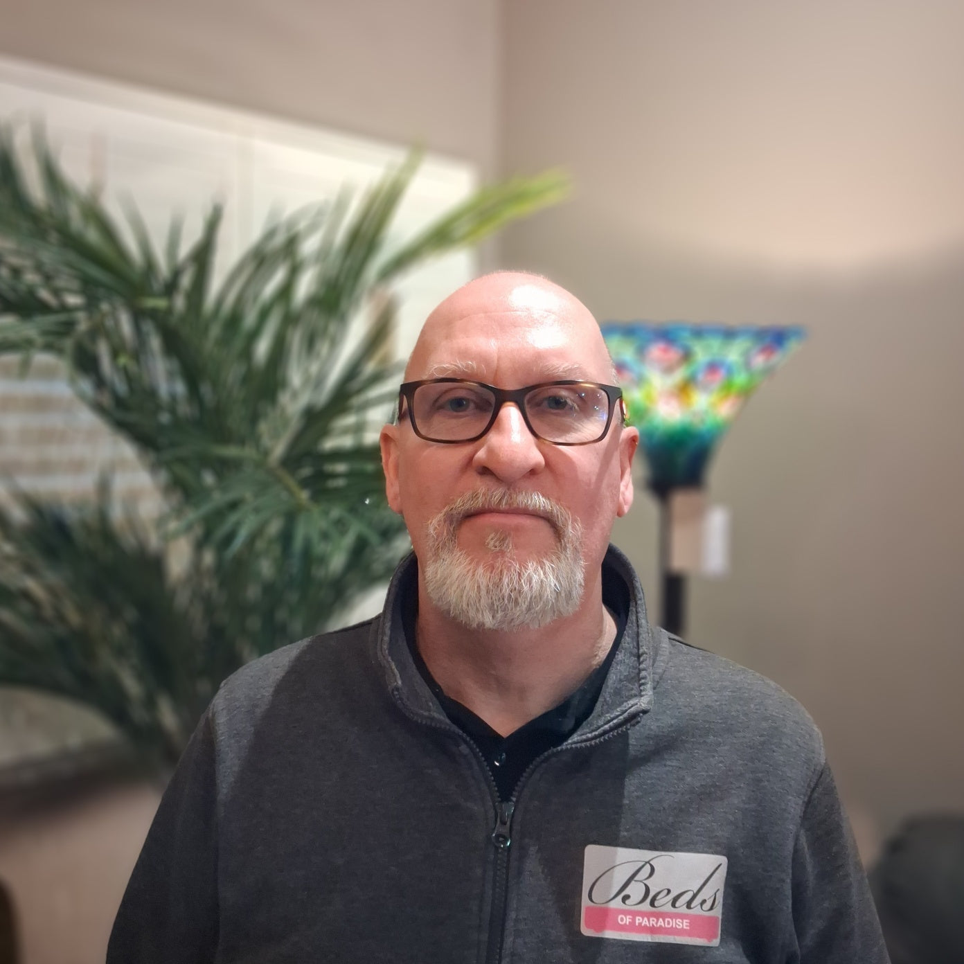 Man wearing glasses and a gray jacket with a name tag in an indoor setting