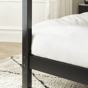 Close-up of a black metal bed frame with white mattress on a light-colored rug.