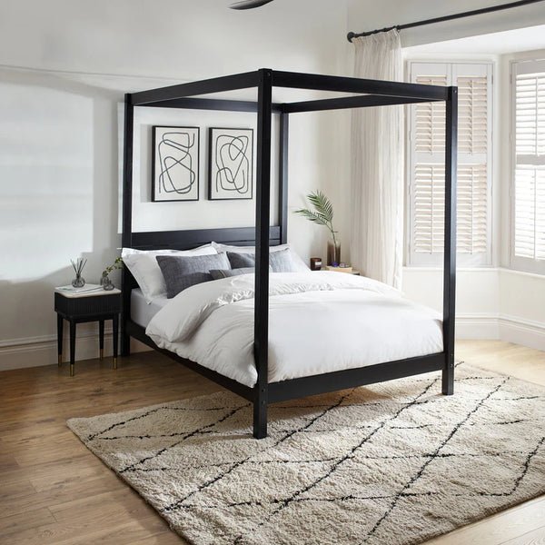 Black canopy bed in a modern bedroom with abstract art and a rug.