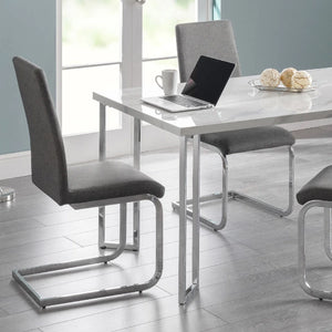 Modern dining area with a white table and gray chairs, featuring a laptop and coffee cup.